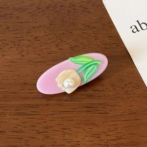 Detailed close-up of pink tulip acetate hair clip with white pearl center on wood