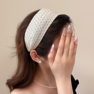 Detailed texture of cream-colored pleated headband with black polka dots on a model