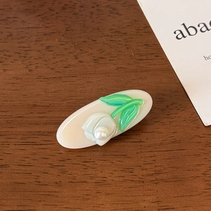 Detailed close-up of a jelly-colored acetate hair clip with floral relief and pearl on wood