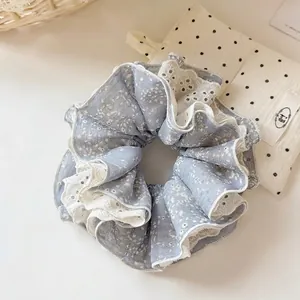 Détail d'un chouchou bleu clair à fleurs avec double bordure en dentelle blanche et plis
