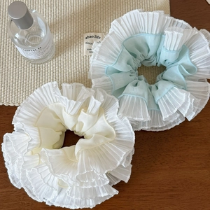 Elegant ruffled pleated scrunchies in cream and light blue displayed on a wooden table