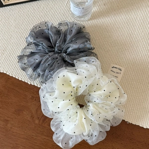 Detail view of grey and beige polka dot organza hair scrunchies on a woven texture mat
