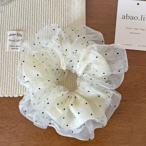 Detailed view of beige polka dot mesh scrunchie with soft pleats on wood surface