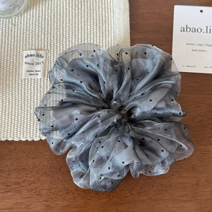 Detail of dark grey polka dot organza scrunchie on a wooden surface for hair styling