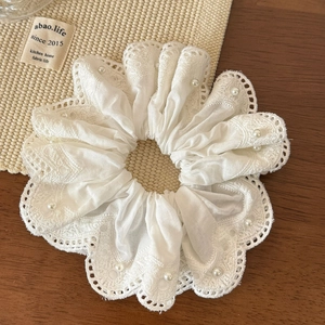 Detail of white lace scrunchie with faux pearls and intricate petal edges on wood