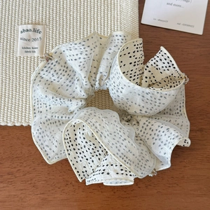 Detail of white polka dot organza scrunchie with delicate bead accents on wooden surface