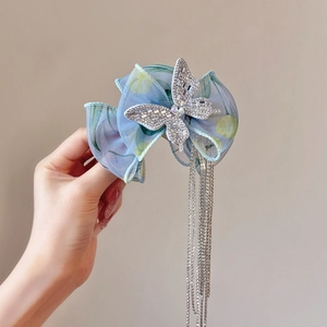 Détail de la pince à cheveux papillon en organza avec strass et longs pompons argentés