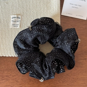 Detail of black polka dot mesh scrunchie featuring elegant crystal bead accents on wood