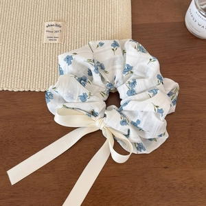 Détail d'un chouchou floral avec ruban crème sur une surface en bois avec des accessoires