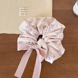 Détail d'un chouchou en mousseline fleurie rose avec un long nœud sur fond en bois