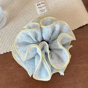 Détail d'un chouchou floral bleu clair avec bordure festonnée jaune sur bois