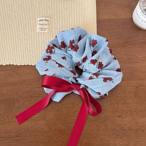 Détail d'un chouchou floral bleu clair avec un grand nœud en satin rouge sur bois