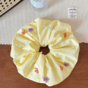 Détail d'un chouchou en tissu jaune avec perles colorées sur une surface en bois