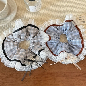 Detail of plaid scrunchies with lace trim, ribbon bows, and metal charms on a desk