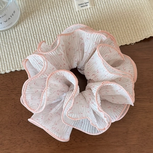 Vue détaillée du chouchou en mousseline blanche avec fleurs roses et bordure ondulée