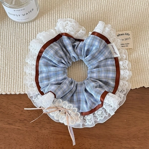 Detail of blue plaid scrunchie with lace trim, ribbon bow, and Good Luck metal charm