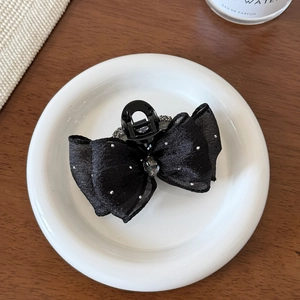Close-up of black bow hair claw with rhinestones on a white ceramic plate and wooden desk