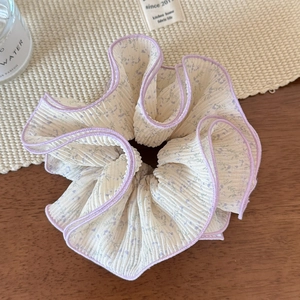 Détail d'un chouchou en dentelle florale avec bordure violette et texture en mousseline