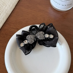 Detailed close-up of a black tulle bow hair claw with sparkling rhinestones on a white plate