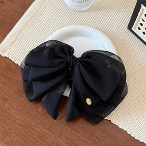 Detail of multi-layered black organza bow hair clip with elegant gold logo plate