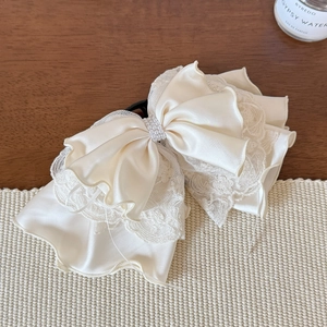 Close-up of elegant lace bow hair claw clip with pearls on a creamy satin fabric