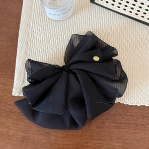 Detail of a large black sheer tulle bow hair clip with a golden oval metal brand tag
