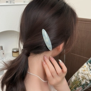 Pince à cheveux élégante en acétate marbré bleu clair avec lettrage doré sur modèle