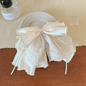 Detail of elegant cream satin bow hair clip with lace edges and small pearl accents