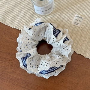 Detail of blue gingham and white lace hair scrunchie shown with luxury perfume bottle