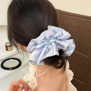 Chouchou élégant en satin bleu clair avec nœud et perle porté sur un chignon bas chic