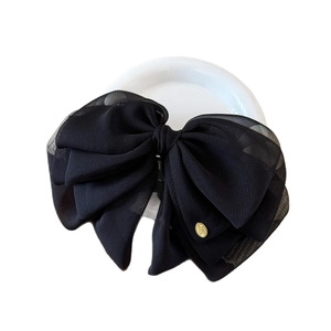 Elegant large black oversized tulle bow hair clip with a gold metal brand tag on white