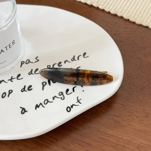 Détail de barrette en acétate écaille de tortue avec lettrage doré sur assiette blanche