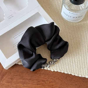 Detail of elegant black satin scrunchie with sparkling grey beads on textured background