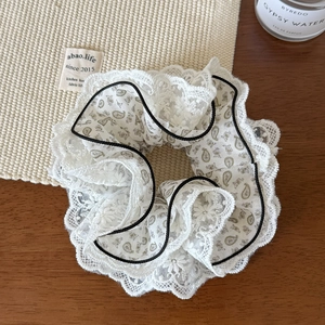 Close-up of elegant four-layer lace scrunchie with paisley pattern and black piping