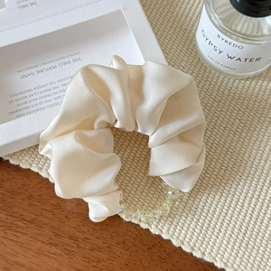 Detailed close-up of cream satin scrunchie with sparkling beads on a textured surface