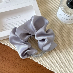 Close-up of grey satin scrunchie with crystal beads on a textured woven mat backdrop