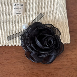 Détail d'une pince à cheveux rose en organza noir avec perle blanche et rubans fins