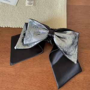 Detail of premium silver textured fabric and black satin bow hair clip on a wooden desk