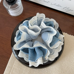 Detail view of large blue chiffon hair scrunchie with white lace edges on a tray