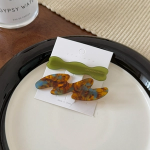 Close-up of olive green and tortoiseshell acetate wave hair clips on a white display card