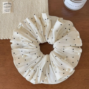 Close-up of beige chiffon scrunchie with black polka dots and pearls on a wooden desk