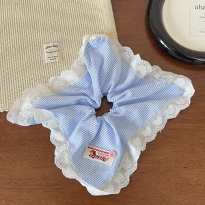 Détail d'un chouchou à rayures bleues avec bordure en dentelle cœur et étiquette tissée