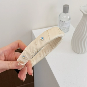 Détail d'un serre-tête en satin crème orné de perles et de fleurs en strass