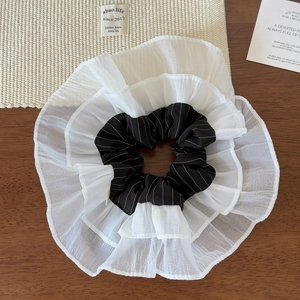 Close-up of a black striped scrunchie with layered white mesh ruffles on wood background