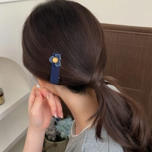 Détail d'une pince à cheveux fleur bleue mate portée sur une queue de cheval basse
