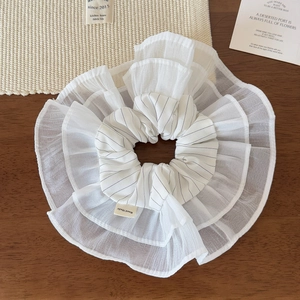 Detail view of a white organza scrunchie with black stripes and a Hand Made label