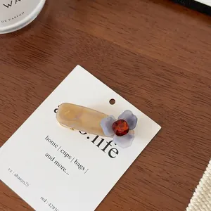 Détail d'une pince à cheveux fleur mate avec résine marbrée et strass rouge brillant
