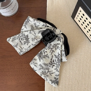 Detail of large floral print bow hair claw clip made of light fabric on a wooden desk