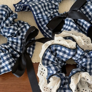 Close-up of blue gingham scrunchie with lace edges and a black satin bow decoration