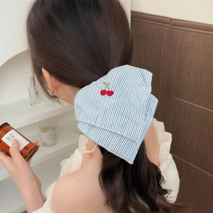 Blue and white striped scrunchie with red cherry embroidery worn by a model